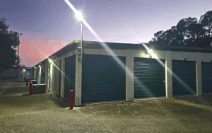 Exterior self-storage units at night featuring bright LED security lighting, green roll-up doors, and paved drive-up access.